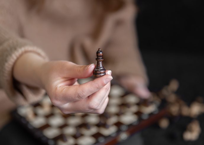 Close up of wooden chess piece in female hands, blurred background.